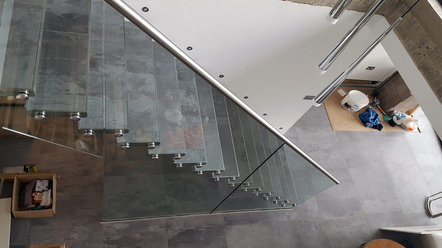 Glass staircase with stainless steel handrails, gray tile steps, and white ceiling.