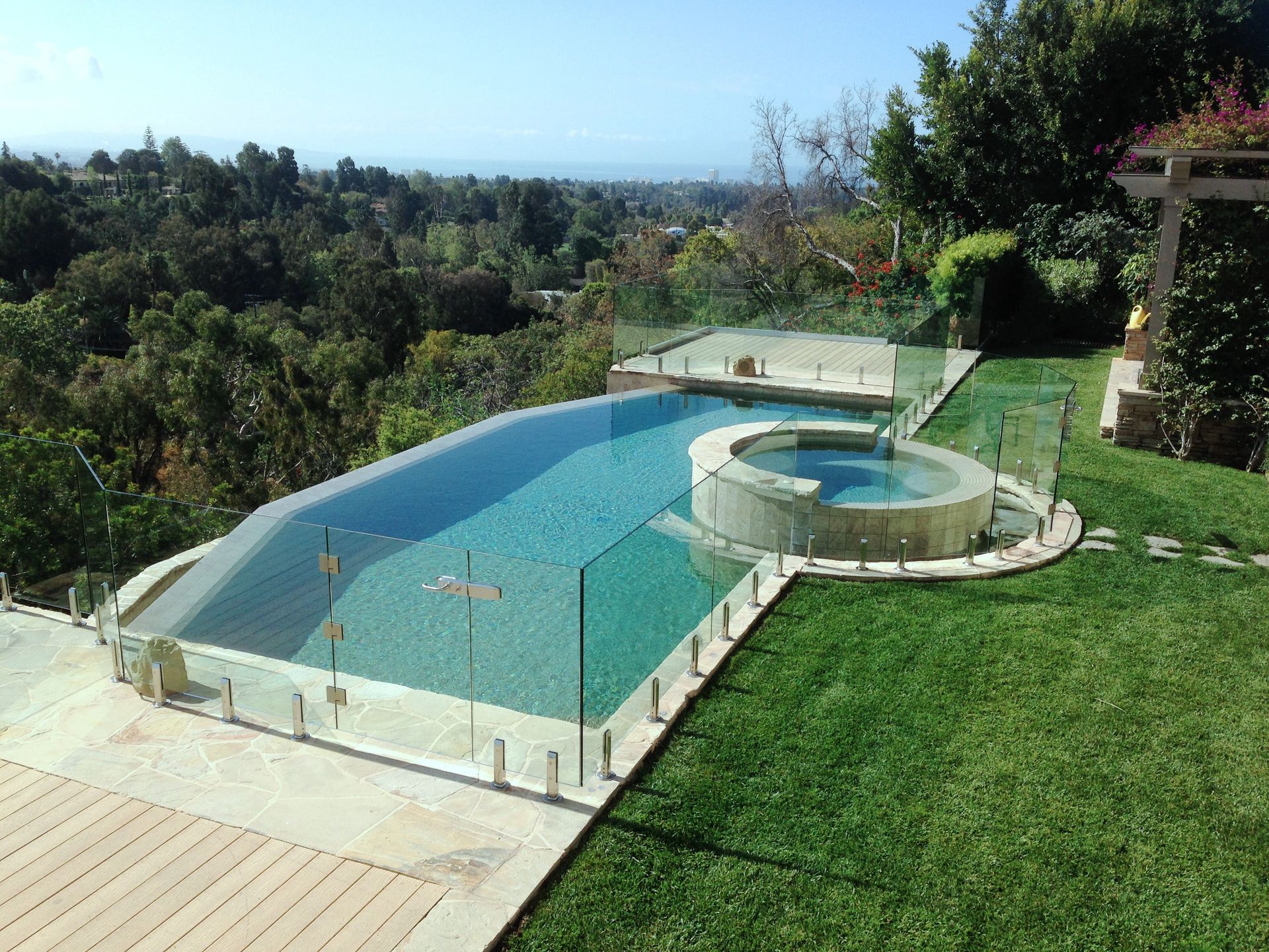 Swimming pool with glass fencing, a hot tub, and a view of trees and the ocean.