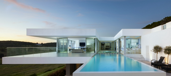 Modern white house with a pool, overlooking a green landscape.