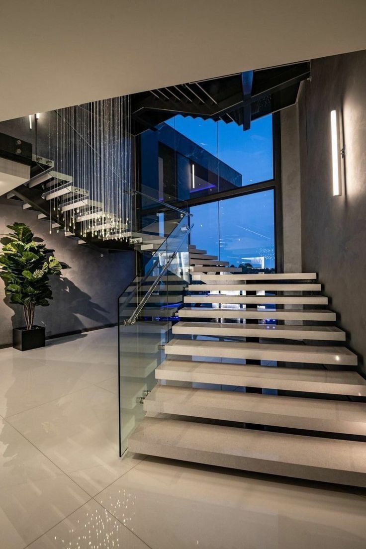 Modern staircase with glass railing and large window, leading to a second story.