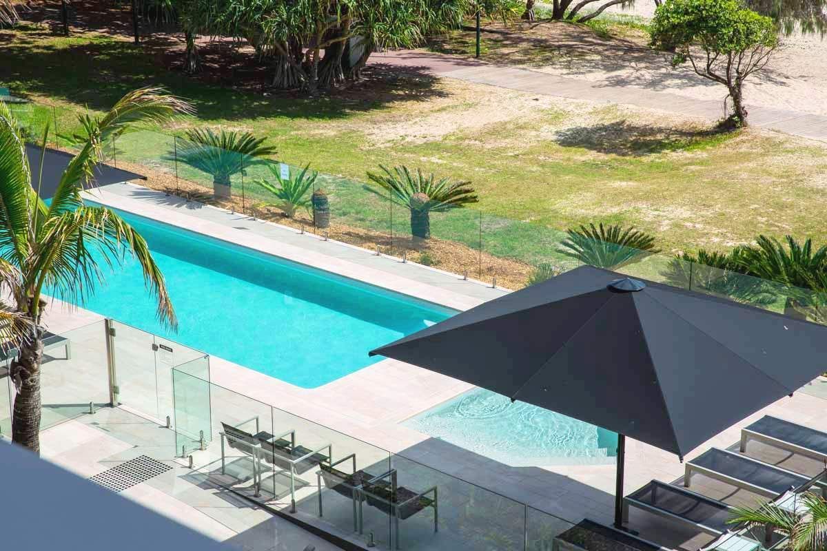 Swimming pool next to a grassy area with palm trees and a black umbrella.