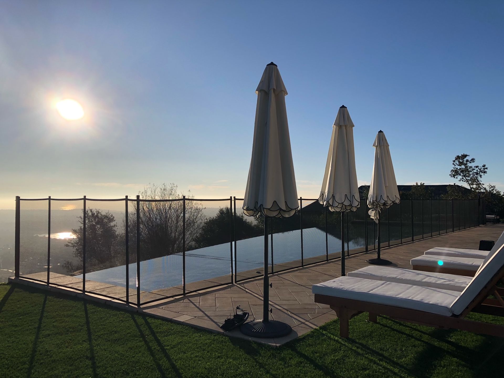 Pool overlooking a vista, with closed umbrellas and lounge chairs on the lawn; sunny day.