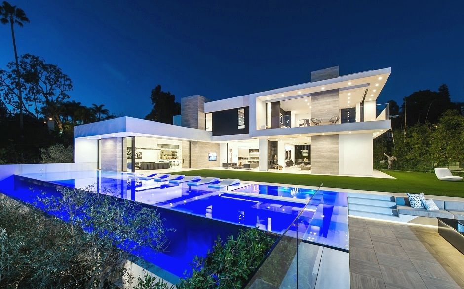 Modern luxury home with illuminated blue pool at night.