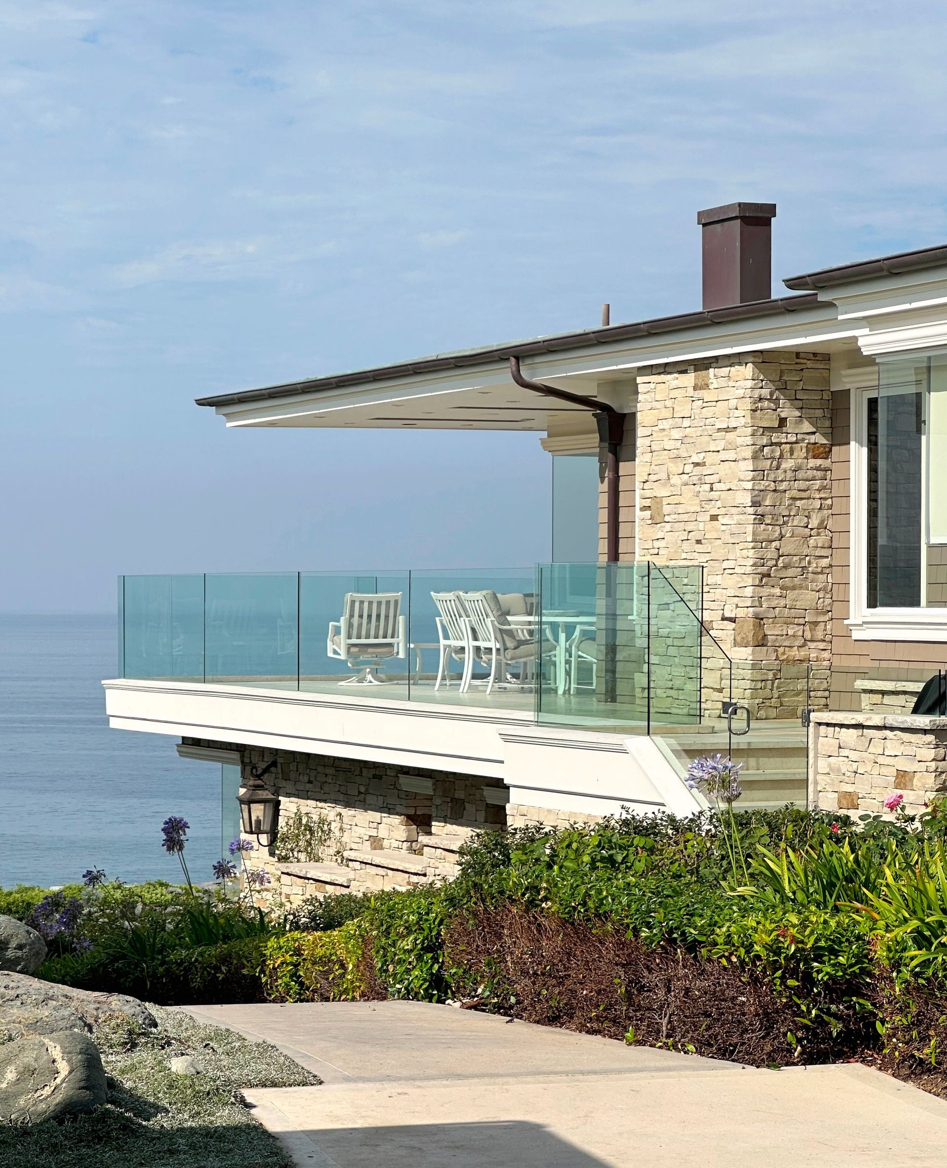 Stone house with glass balcony overlooking the ocean; sunny day.