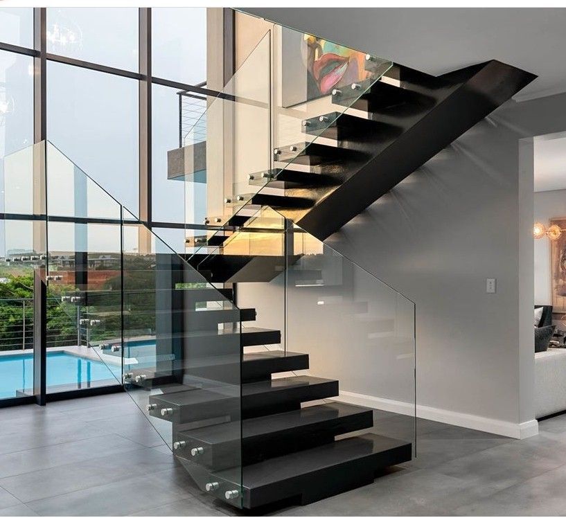 Floating staircase with dark treads and glass railing next to large windows overlooking a pool.
