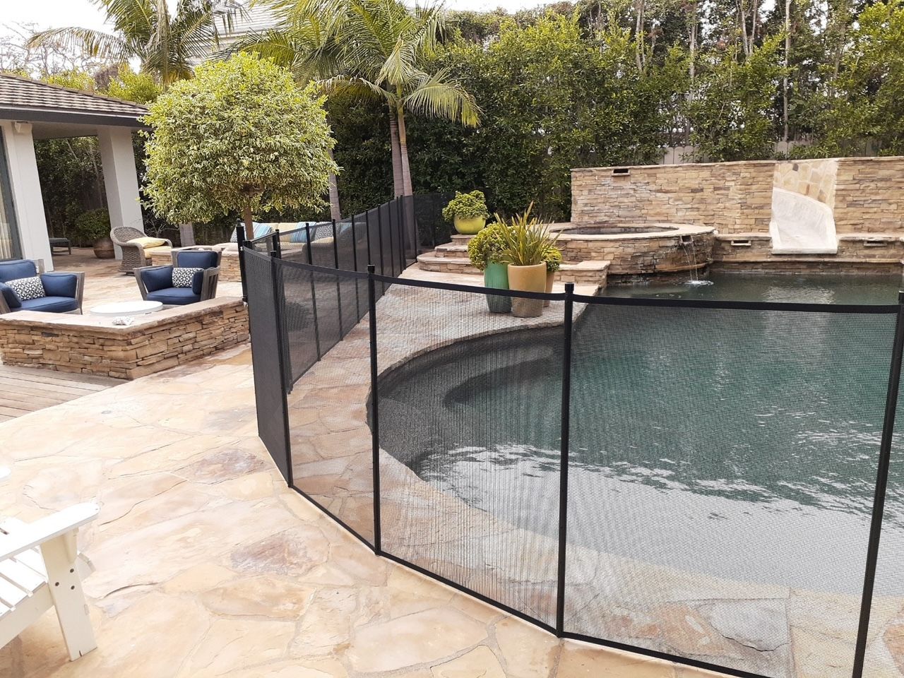 Black mesh pool safety fence surrounds a swimming pool and spa. Outdoor patio furniture nearby.