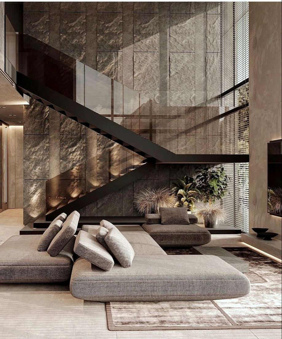 Modern living room with stone wall, black staircase, and grey sectional sofa.