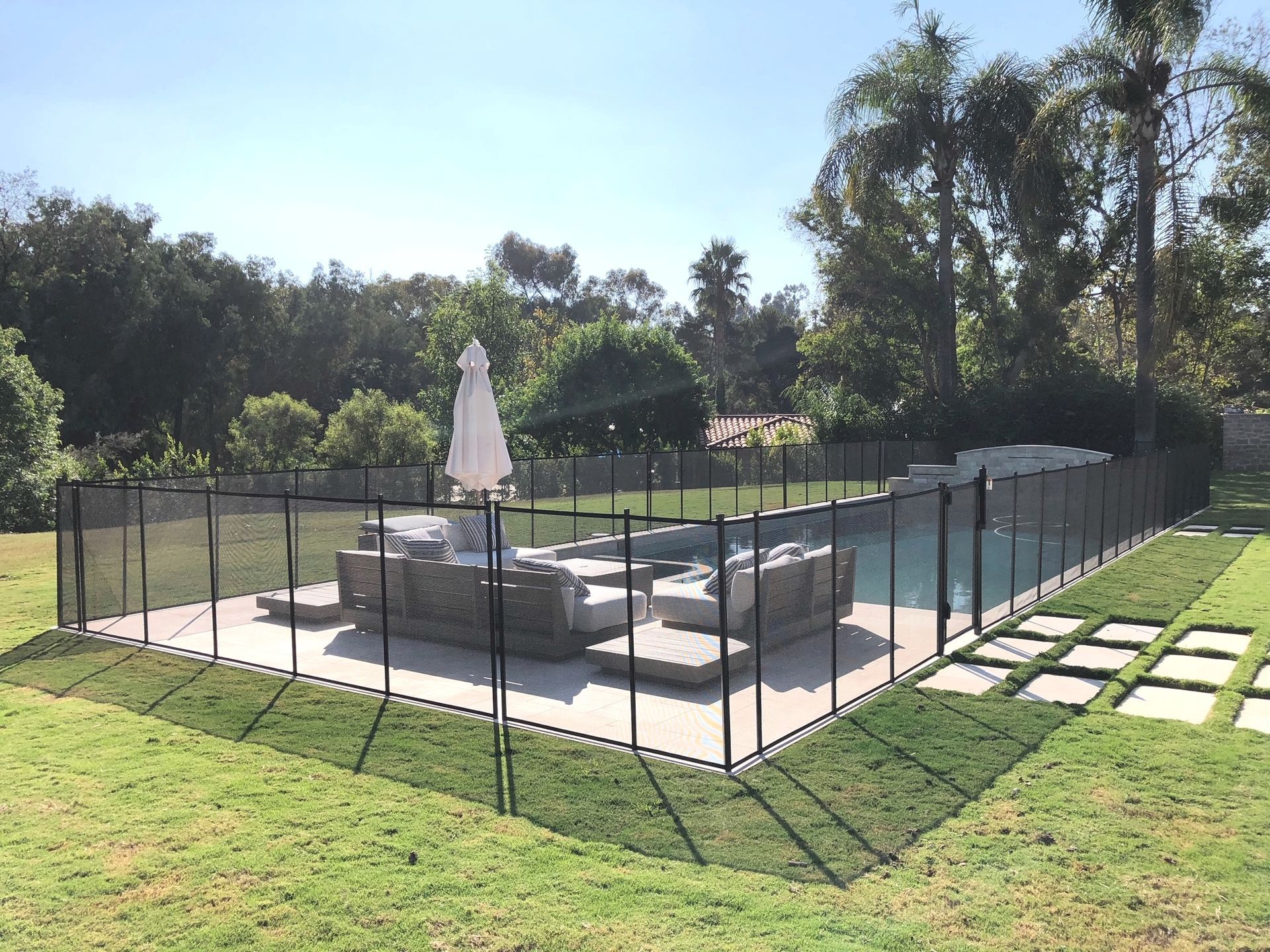 Black mesh pool fence surrounding a pool with patio furniture on a sunny day.