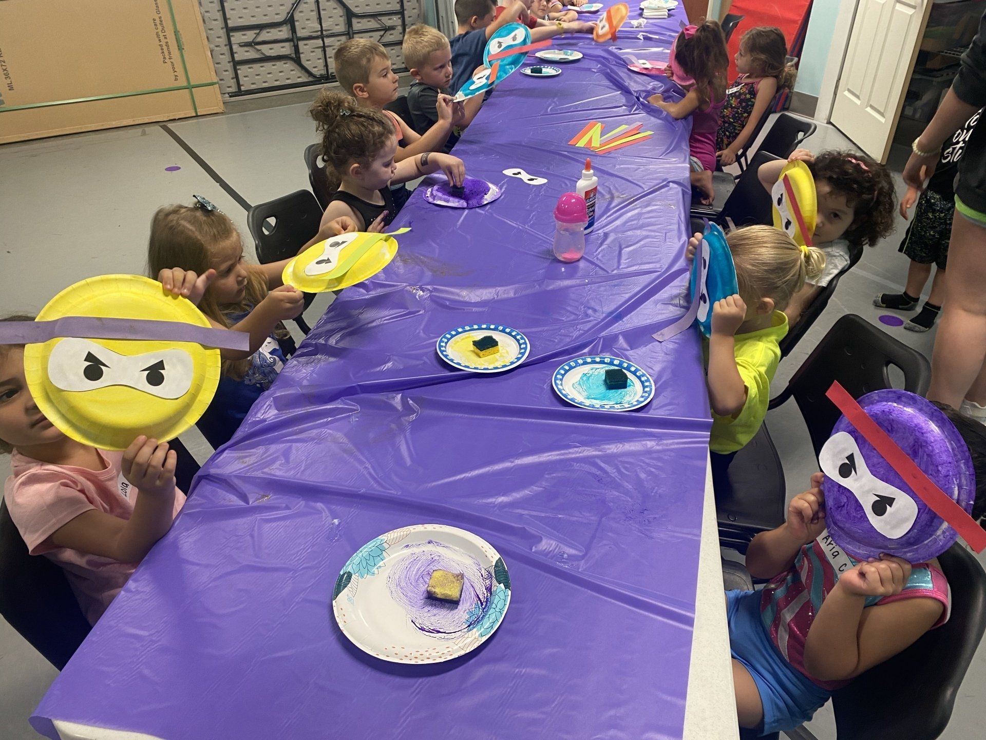 Kids at a crafting table making ninja turtle masks with paper plates and markers.