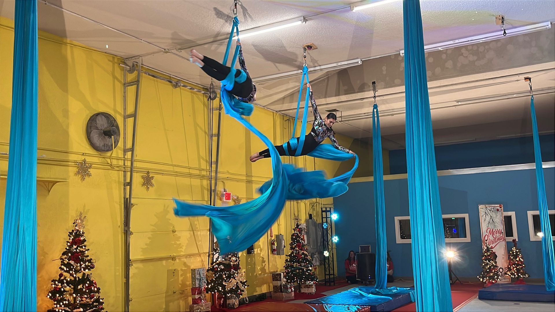 Woman performing aerial silk dance, red fabric, smiling, blue sky background.