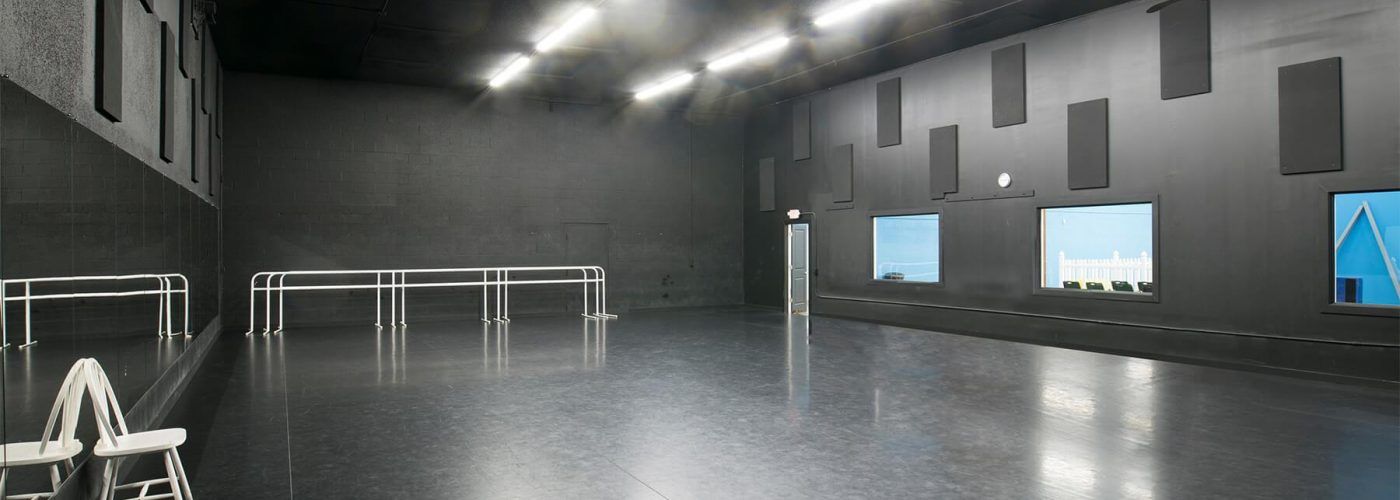 Dark room with shiny floor, windows, and rectangular panels on walls. Some metal railings.