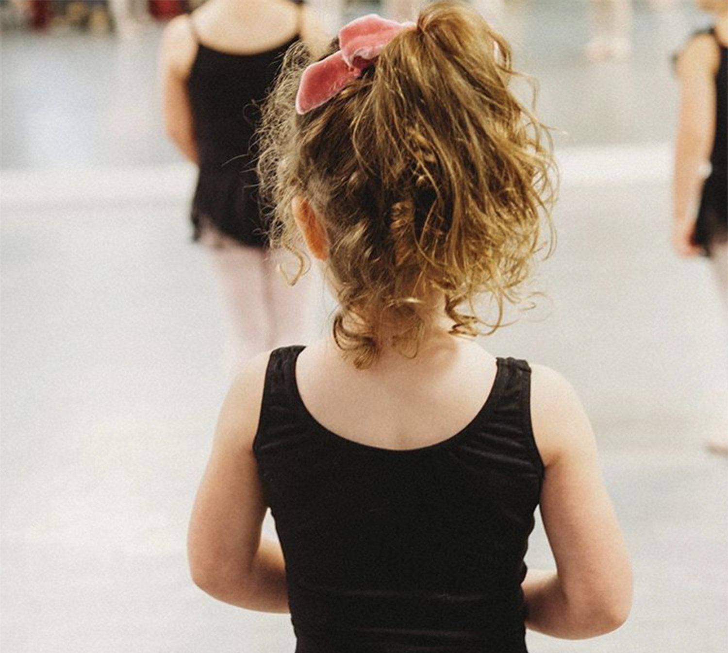 Girl in black leotard with pink bow in hair watches ballet class.