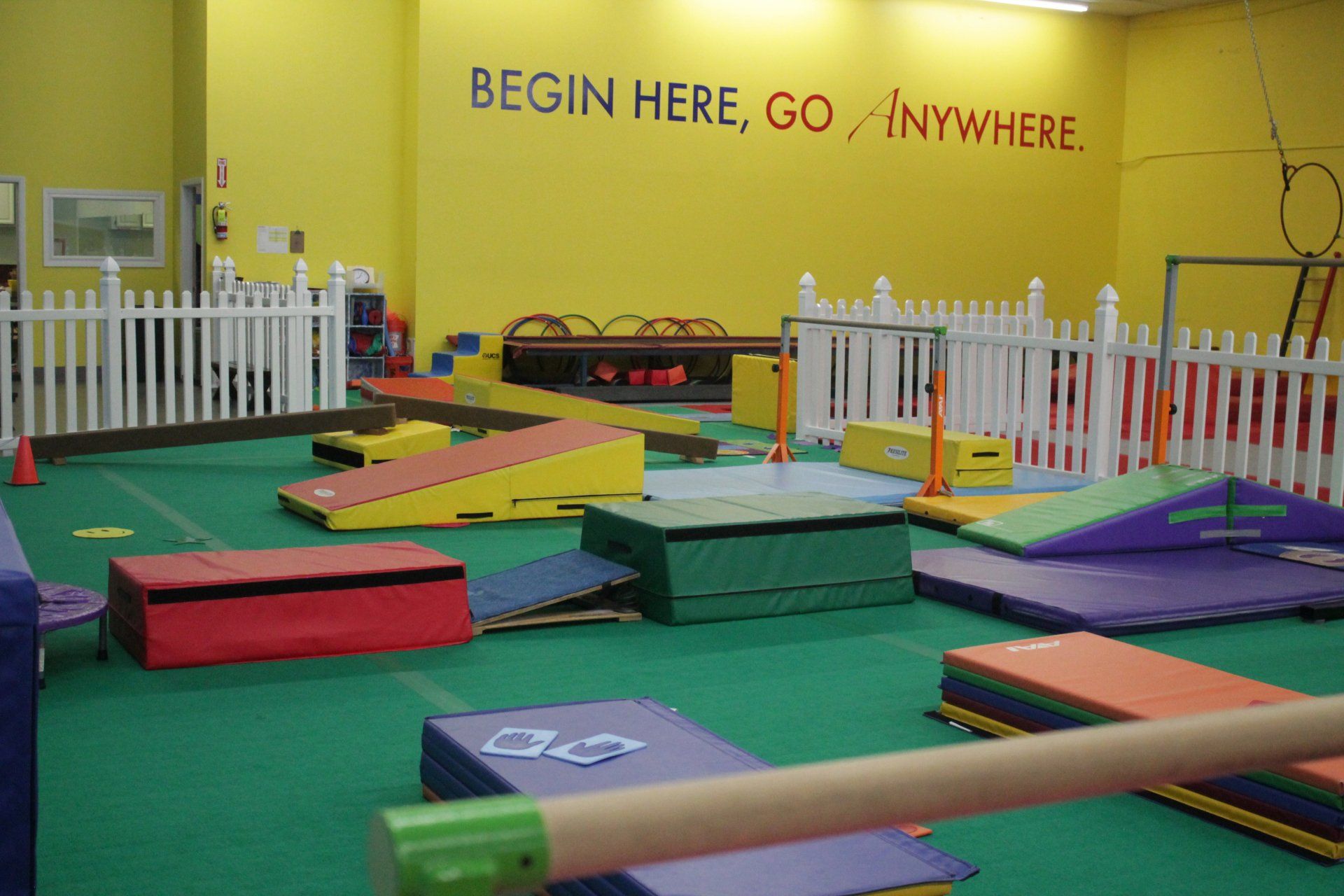 Gymnasium with colorful mats, balance beams, and obstacles. Yellow wall with