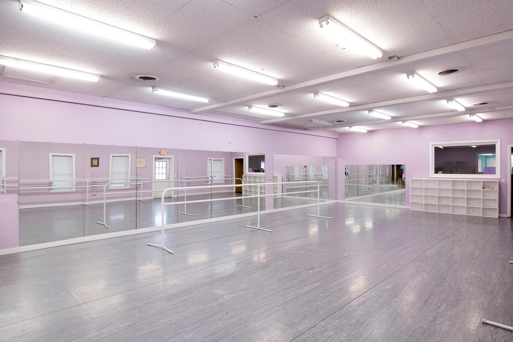 Dance studio with mirrors, ballet barres, and a gray floor, painted light purple.