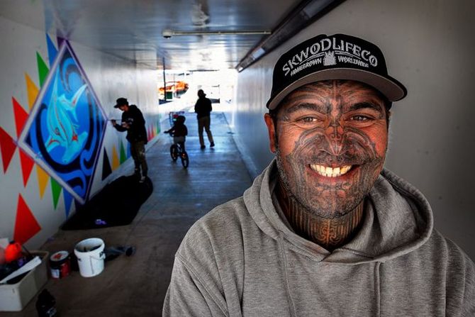 A man with tattoos on his face is smiling in a tunnel.