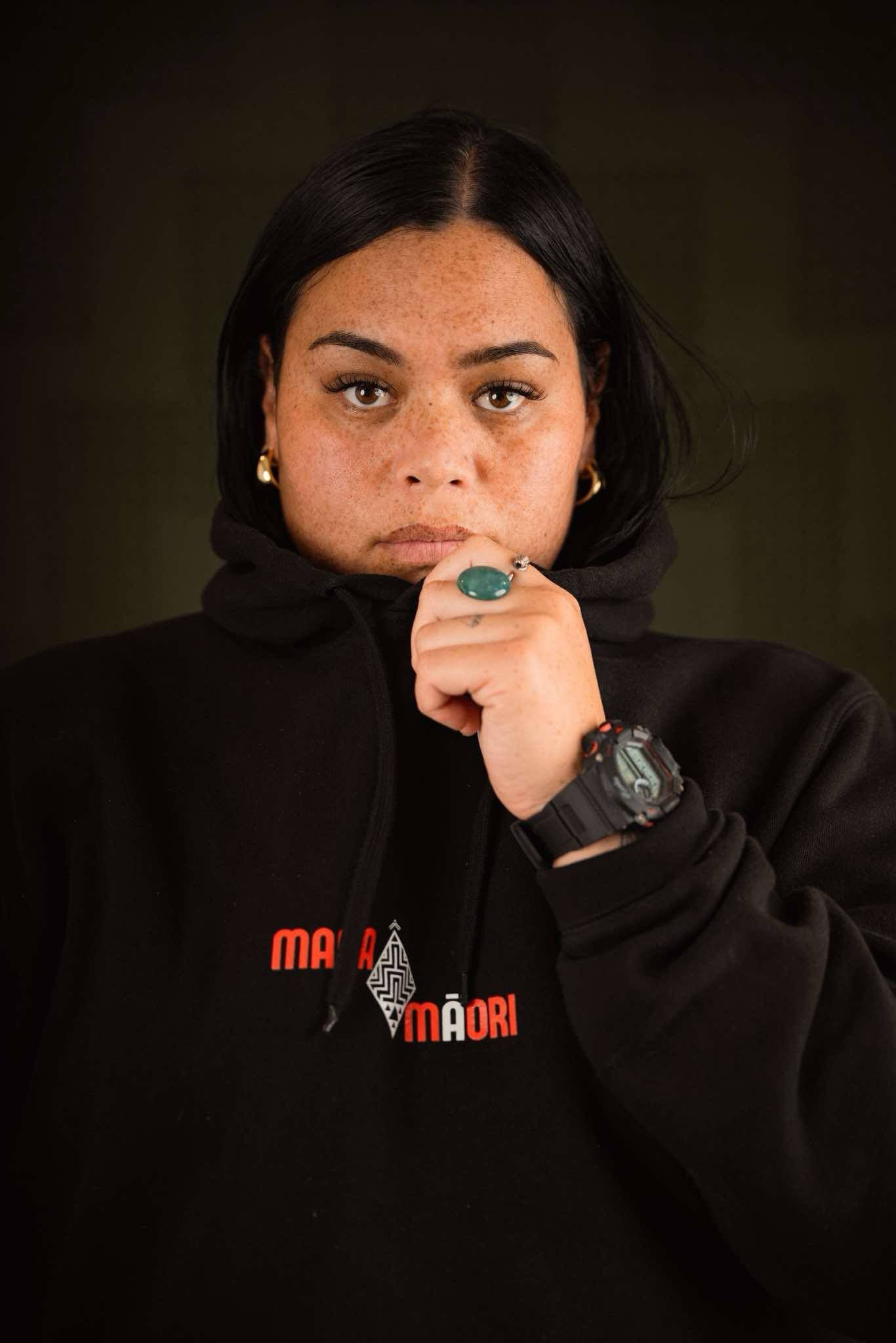 A woman wearing a black hoodie and a watch is covering her mouth with her hand.