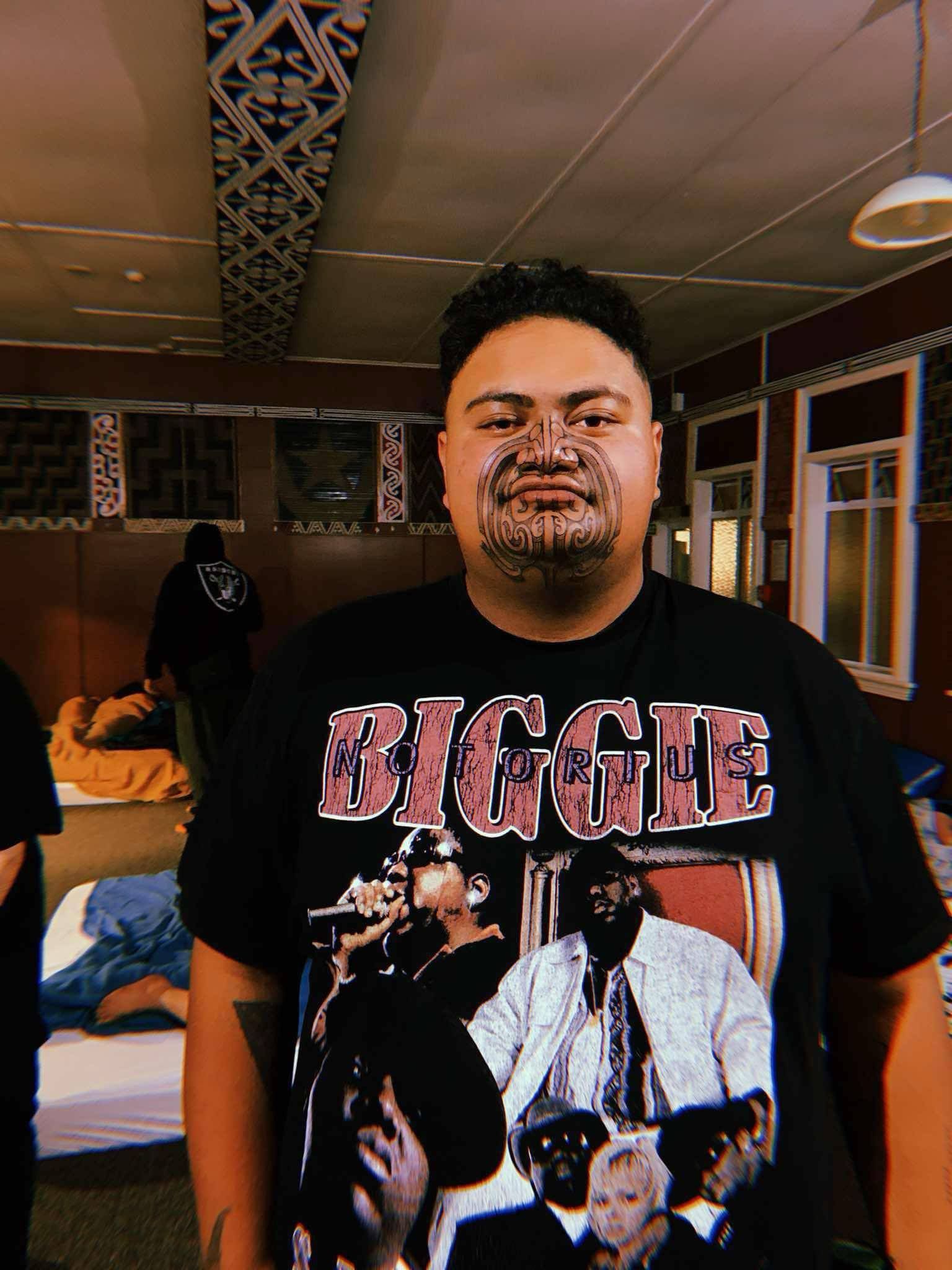 A man with a tattoo on his face is wearing a biggie t-shirt.