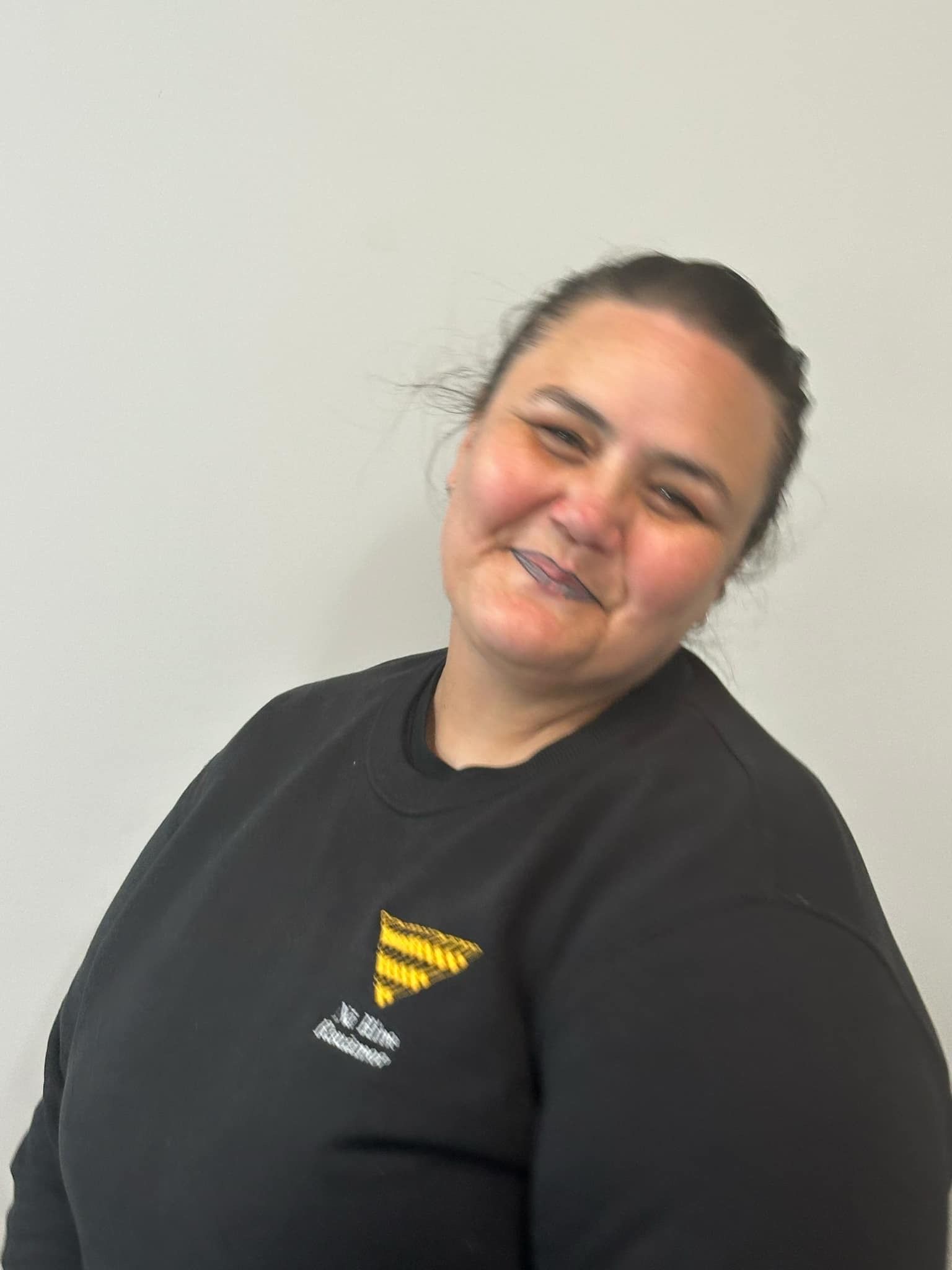 A woman wearing a black sweater with a yellow triangle on it is smiling.