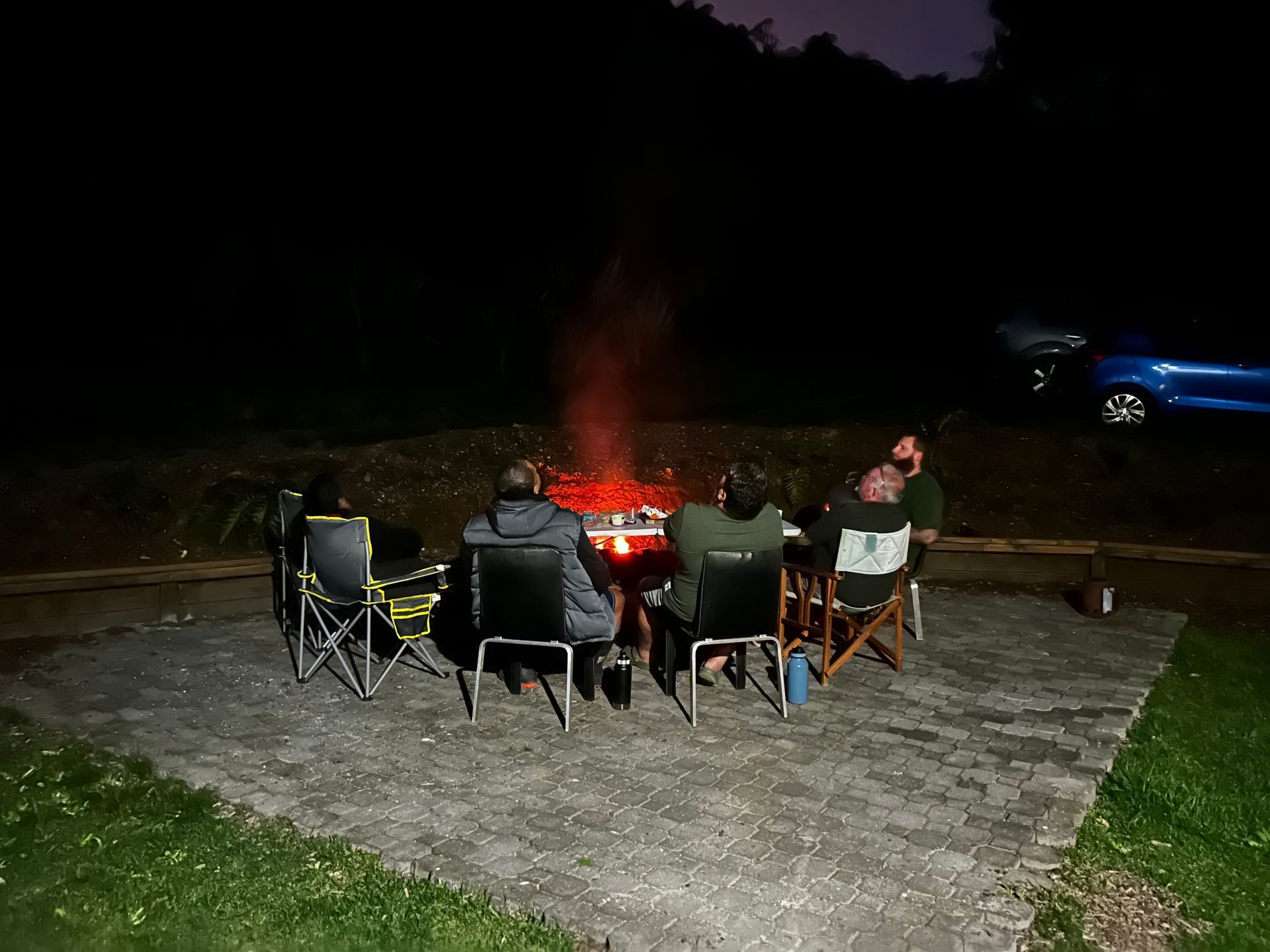A group of people are sitting around a fire pit at night.