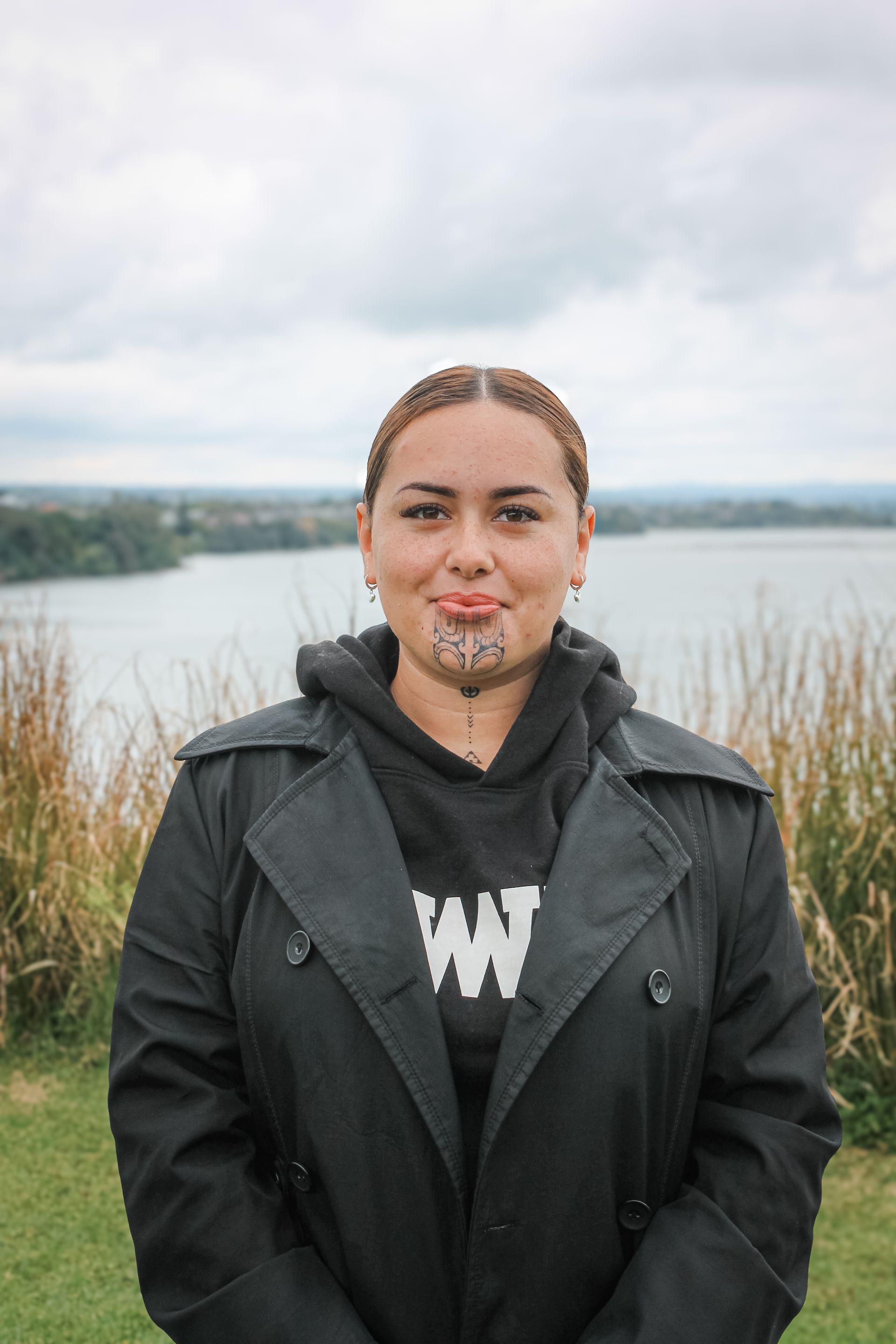 A woman with a tattoo on her face is standing in front of a body of water.