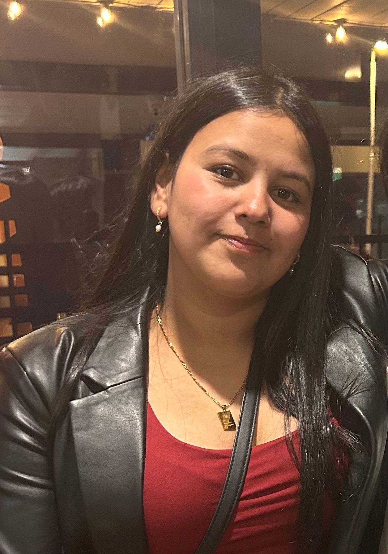 A woman wearing a leather jacket and a red shirt is looking at the camera.