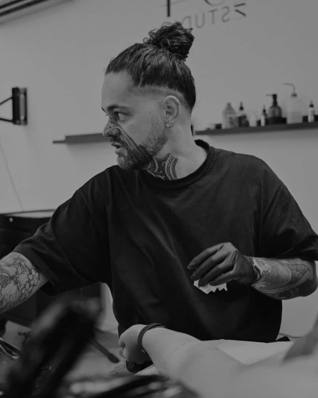 A man with a bun on his head is sitting at a table in a black and white photo.