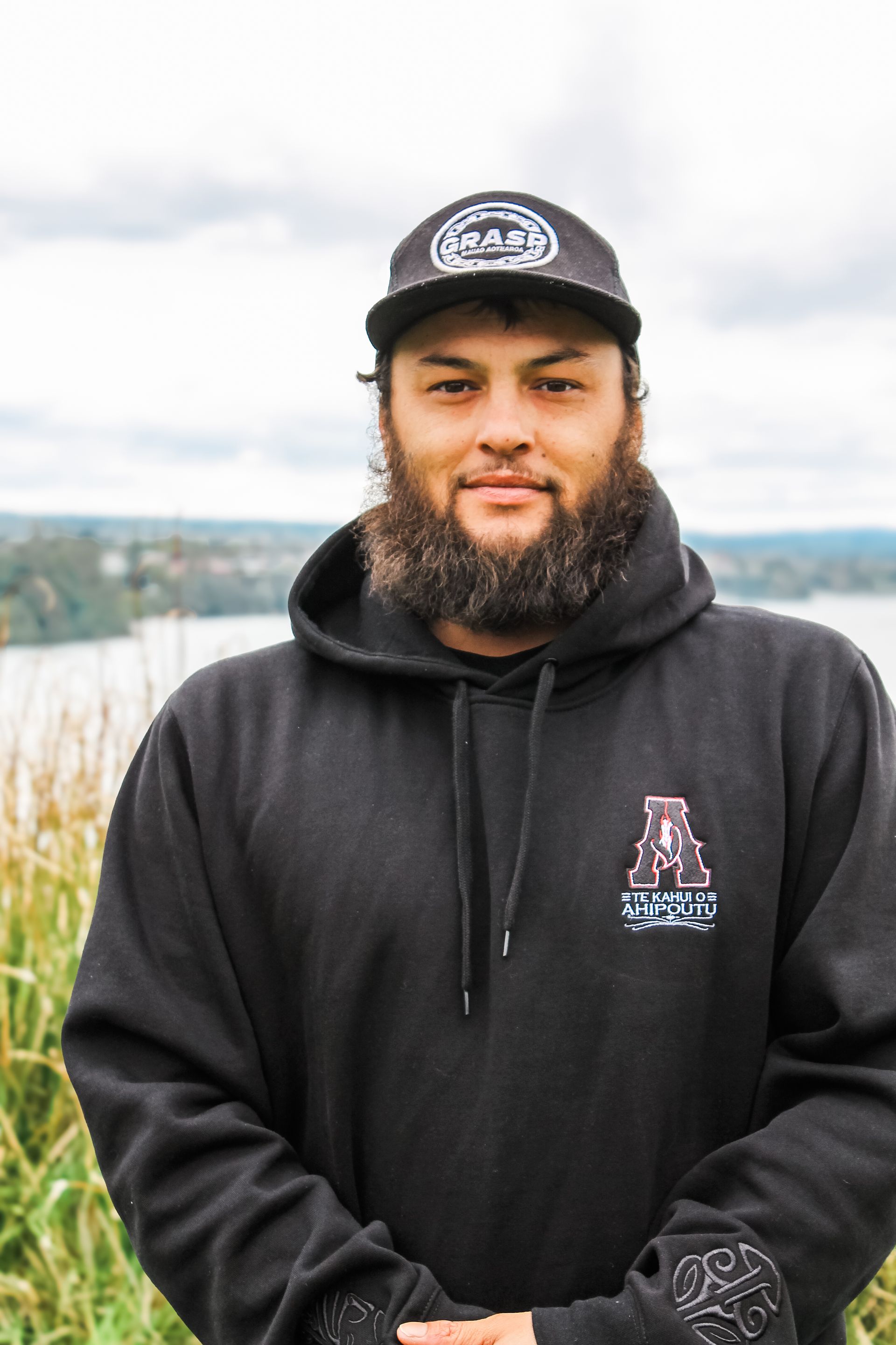 A man with a beard is wearing a black hoodie and a hat.