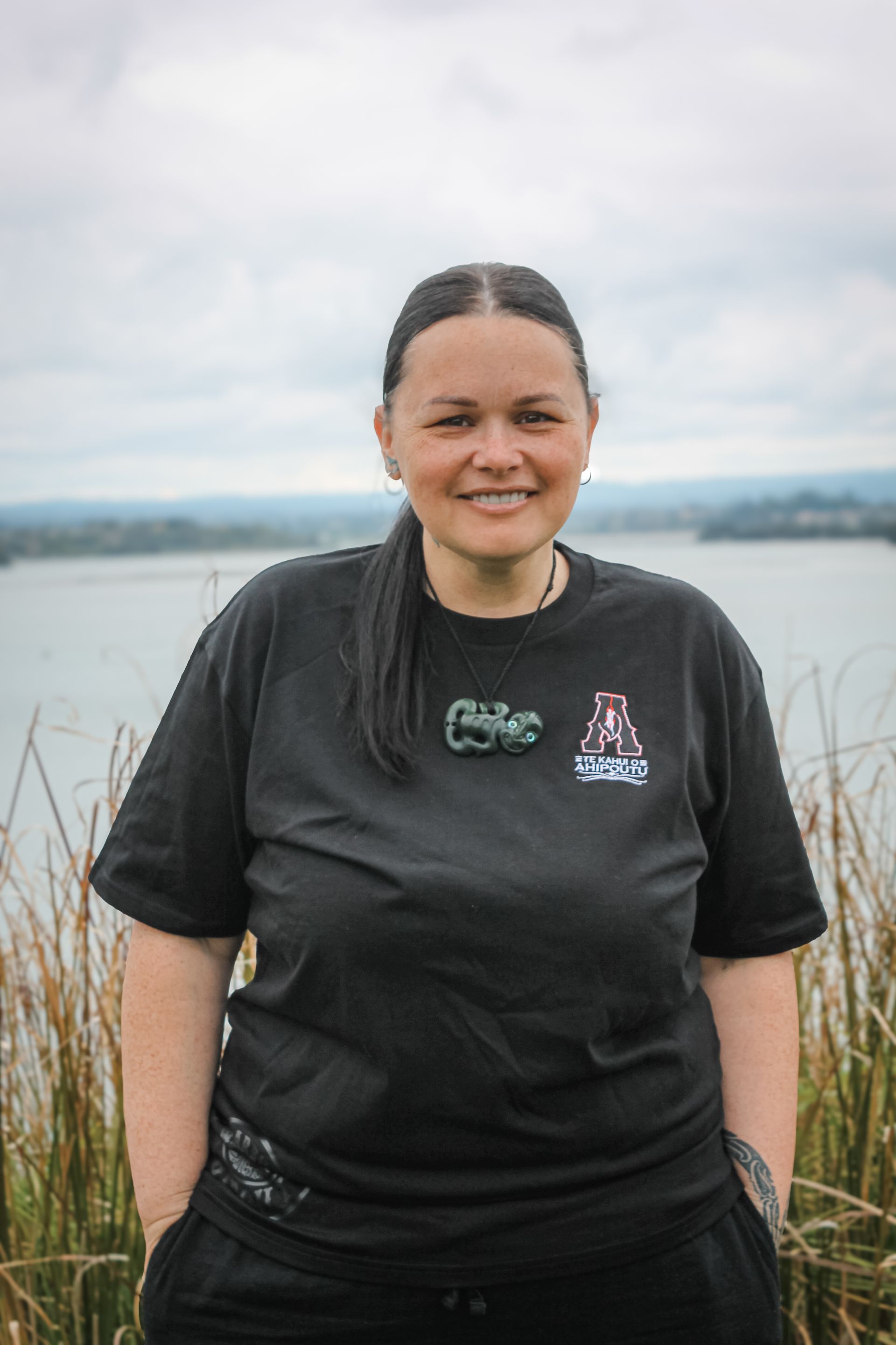 A woman in a black t-shirt is standing in front of a body of water.