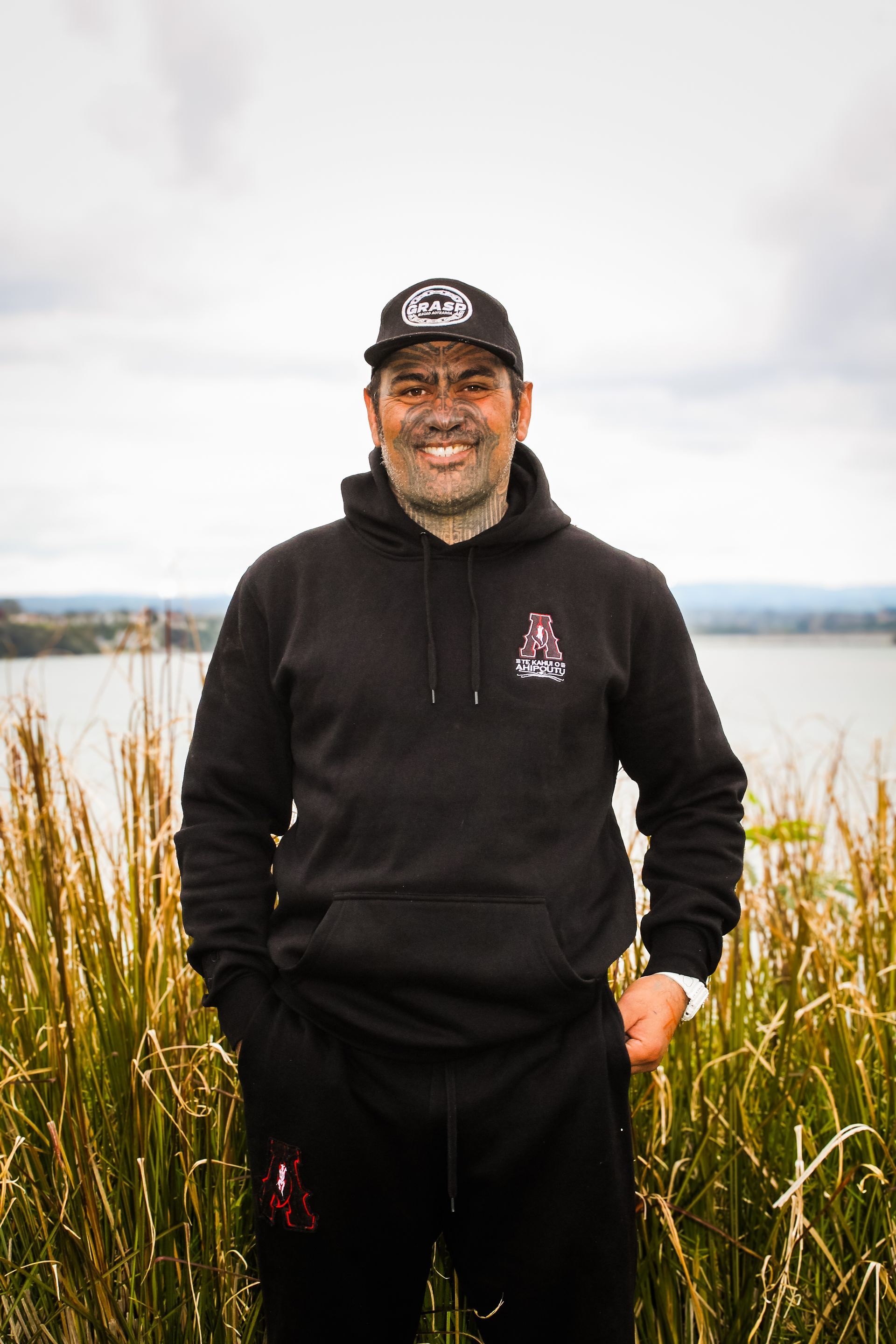 A man in a black hoodie and hat is standing in a field of tall grass.