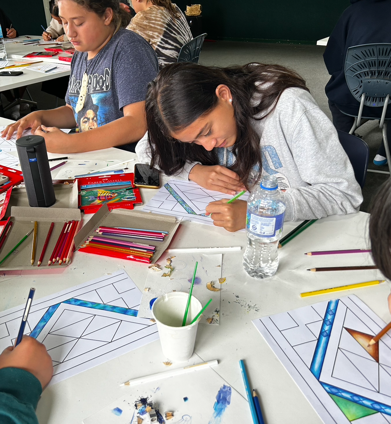A group of people are sitting at a table with pencils and a bottle of water