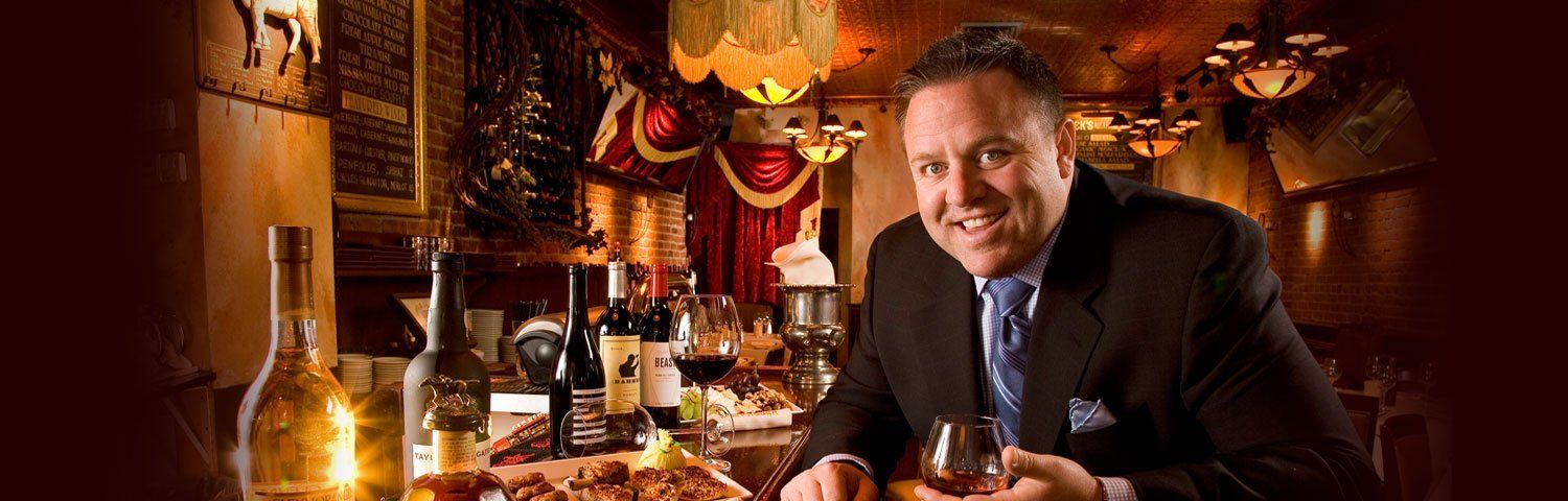 A man in a suit and tie is sitting at a table holding a glass of wine.