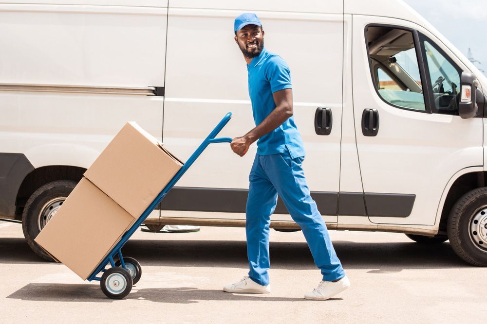 A Delivery Man Is Pushing A Cart With Boxes In Front Of A Van — Express City Couriers in Palm Cove, QLD