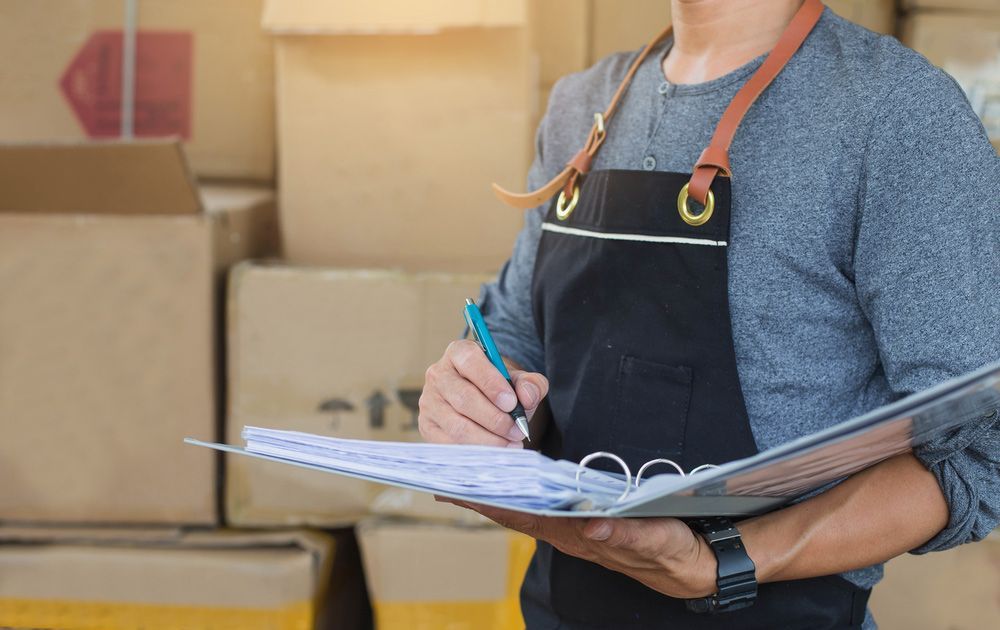 A Man In An Apron Is Holding A Clipboard And A Pen — Express City Couriers in Palm Cove, QLD