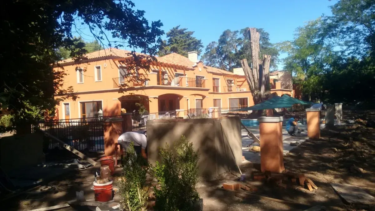 Casa de estuco naranja de dos pisos con balcones, pilares y árboles bajo un cielo azul claro.