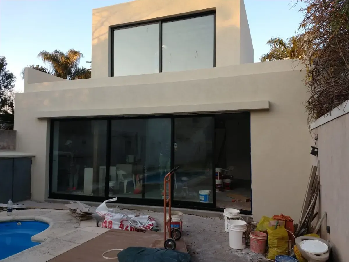 Casa moderna de dos plantas en color beige, con grandes ventanales con marcos negros y piscina. 