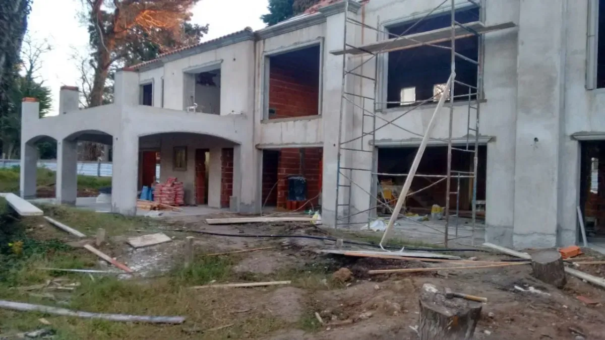 Un edificio de dos pisos en construcción con andamios, con paredes sin terminar y marcos de ventanas abiertos.