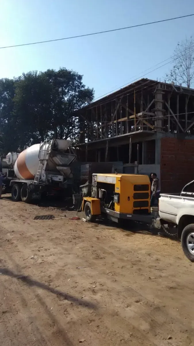 Camión de cemento vertiendo hormigón en una obra. Maquinaria amarilla, edificio a medio construir, camino de tierra marrón.