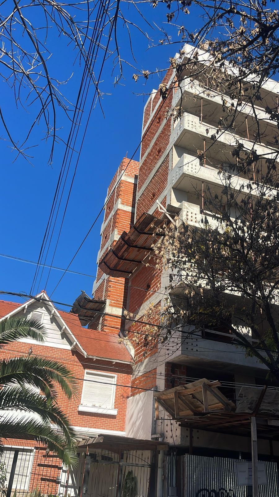 Edificio alto de ladrillo al lado de una casa más pequeña con una ventana blanca contra un cielo azul.