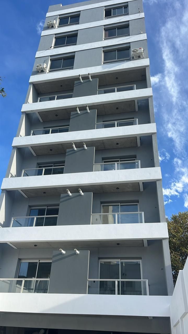 Edificio de apartamentos gris y blanco con balcones contra un cielo azul.