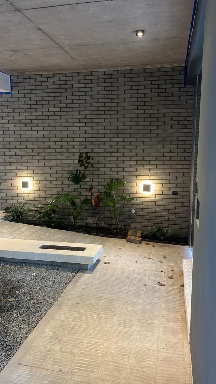 Muro exterior con dos lucernarios cuadrados flanqueando un pequeño parterre; camino de hormigón y grava.