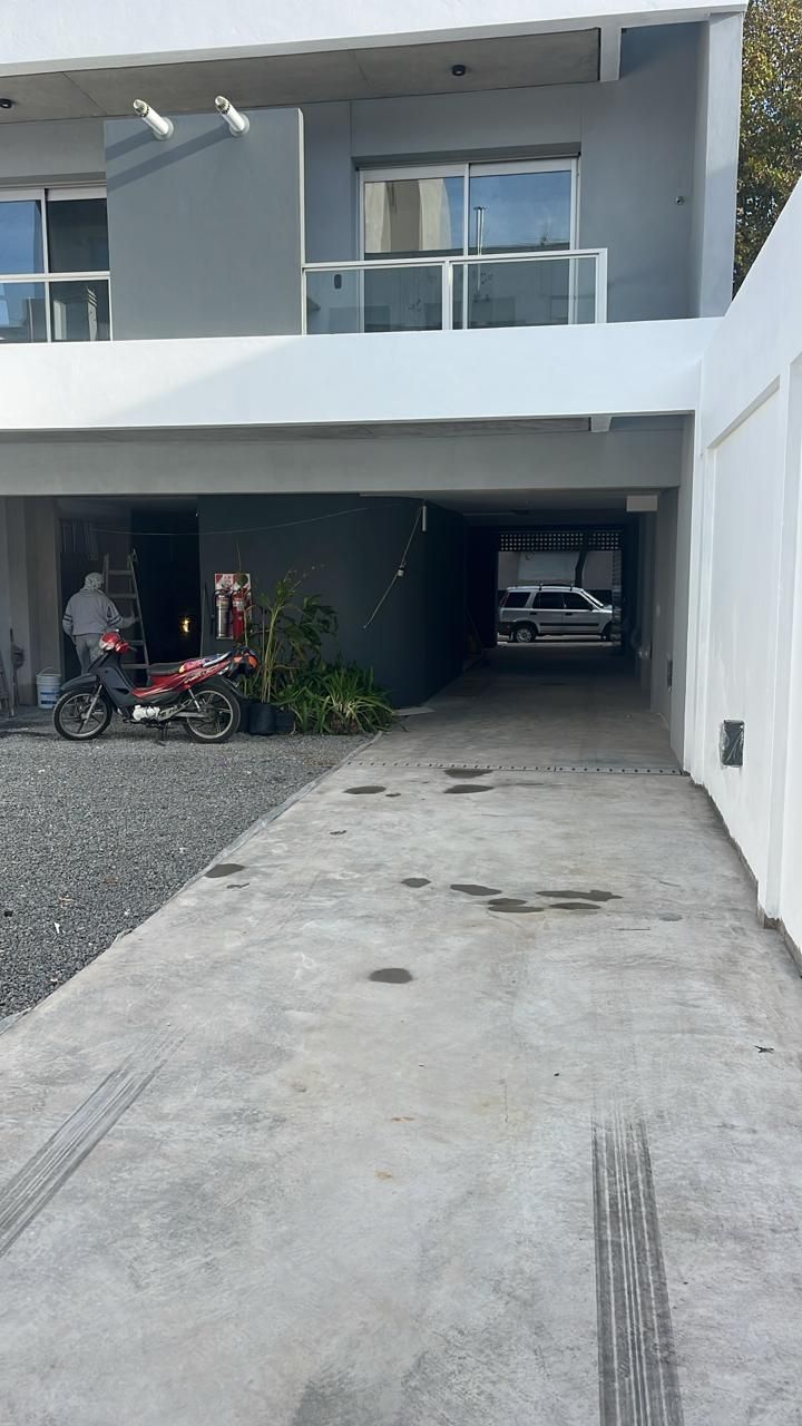 Vista exterior de un edificio moderno de dos pisos con entrada para autos y motocicleta estacionada al costado.