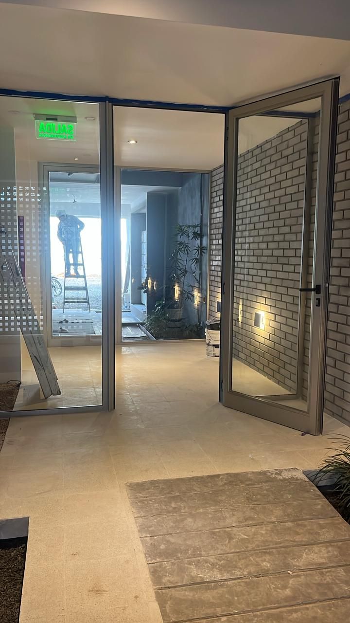 Unas puertas de cristal dan a un pasillo iluminado. A la derecha, una pared de ladrillo blanco.