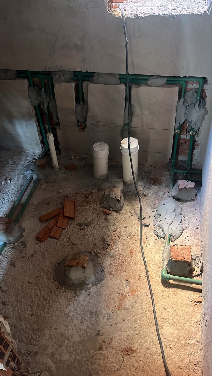 Baño en construcción: tuberías, dos desagües blancos, ladrillo visto, piso y paredes de concreto.