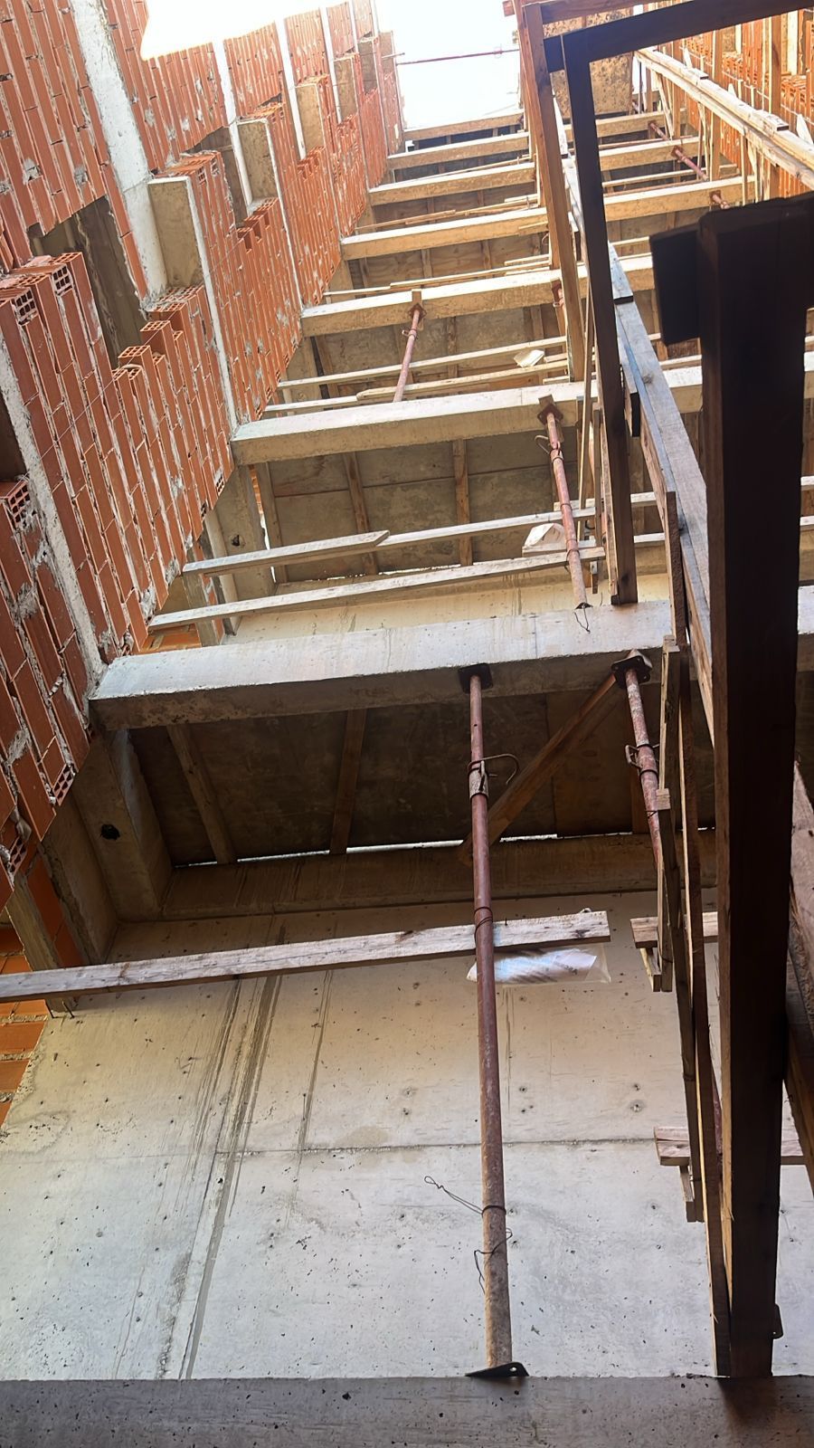 Interior de obra en construcción con paredes de ladrillo y escalera de hormigón en construcción.