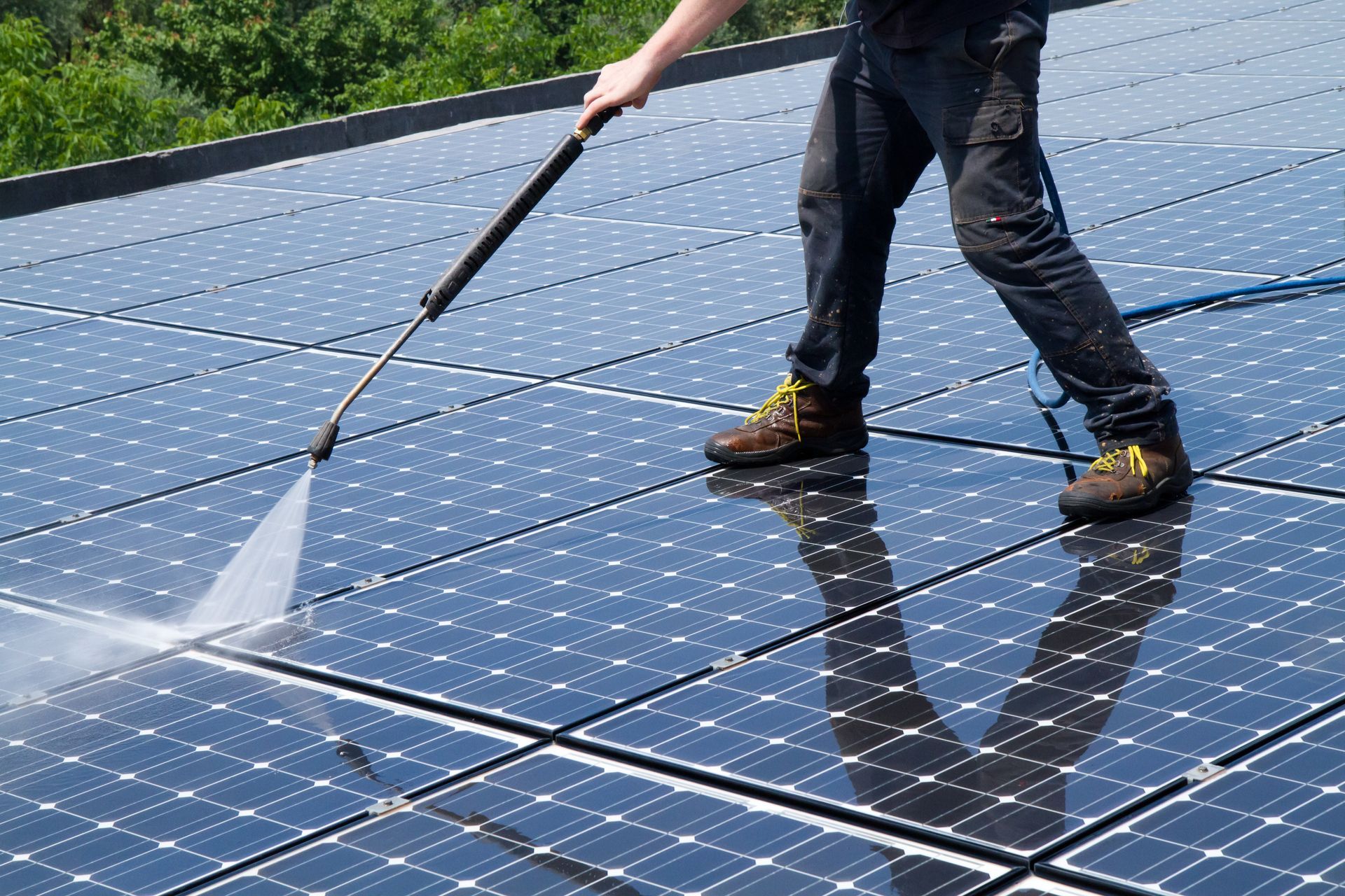 A man is cleaning solar panels on a roof with a high pressure washer.