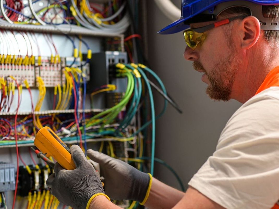 A man wearing a hard hat and goggles is working on a electrical box.