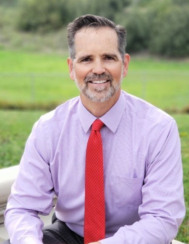 A man in a purple shirt and red tie is smiling