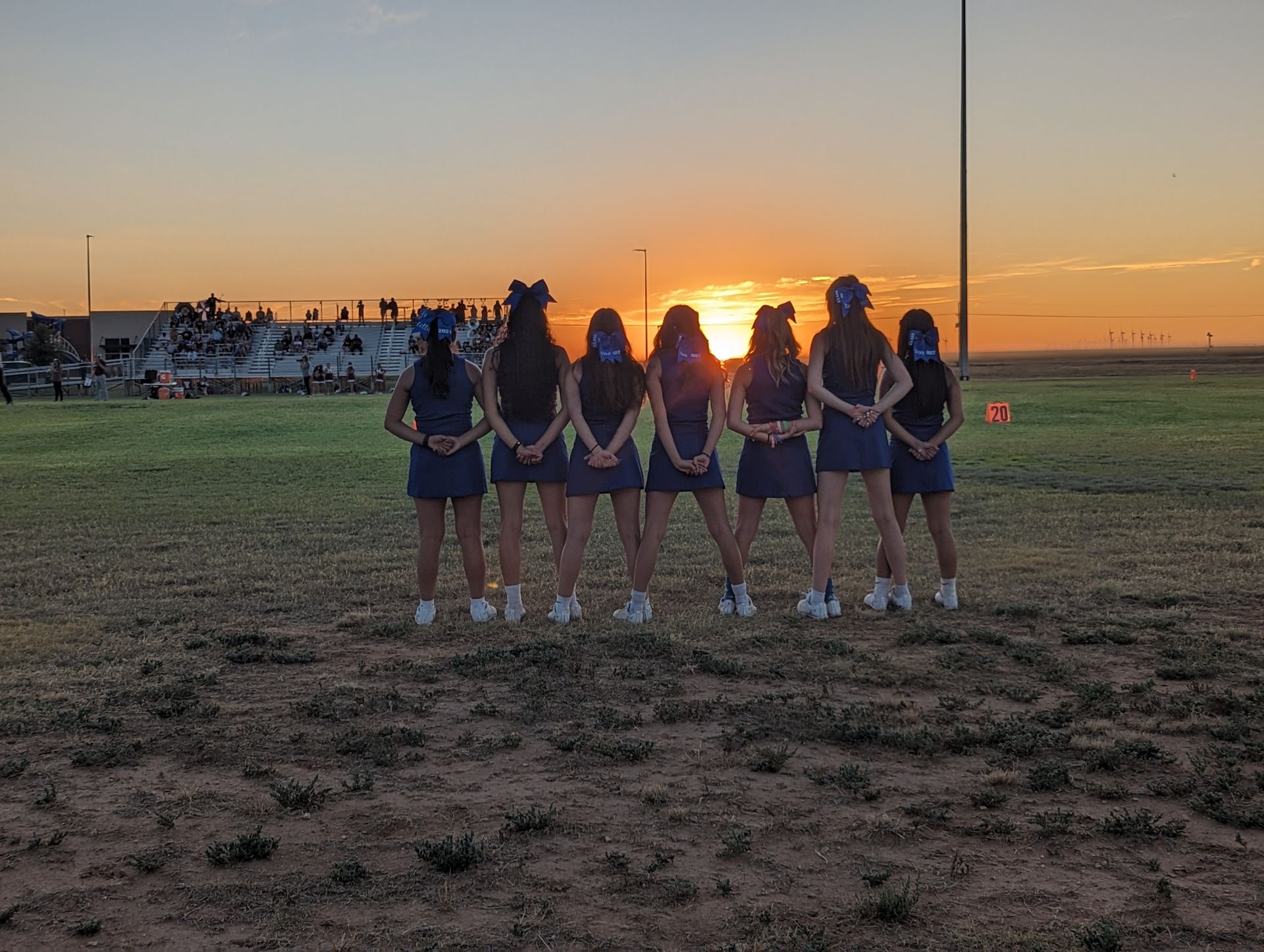 a group of cheerleaders are standing in a field at sunset .