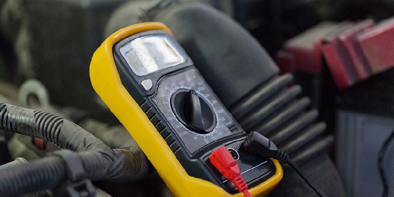 A yellow and black multimeter is sitting on top of a car engine.