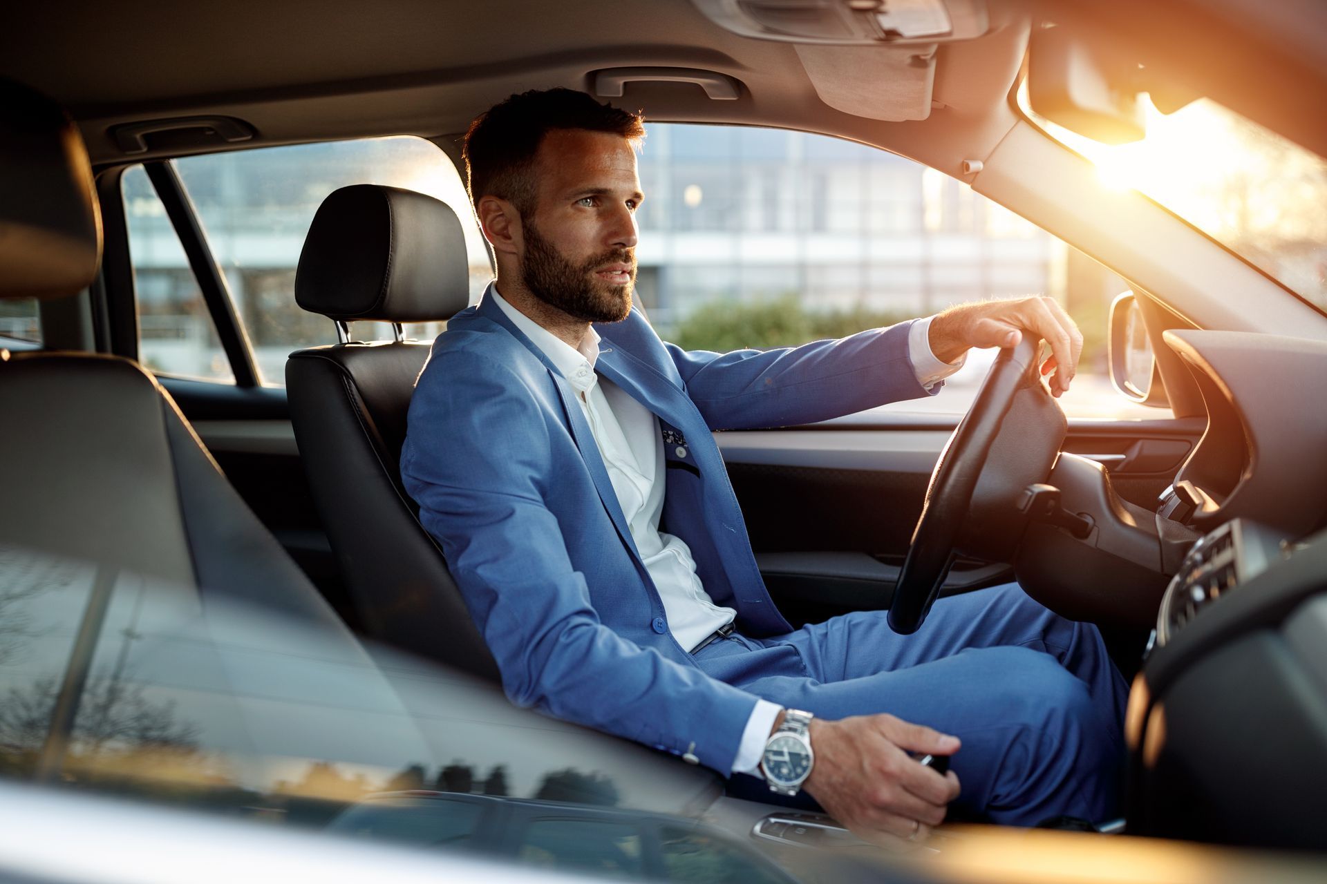 A man in a suit is sitting in the driver 's seat of a car.